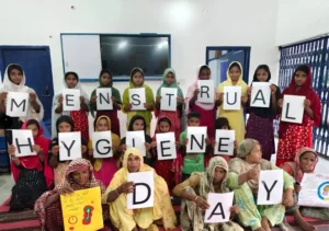 Rural women and adolescent girls holding letters spelling Menstrual Hygiene Day during an awareness workshop by BJUP, a Menstrual Hygiene Awareness NGO in Bihar.
