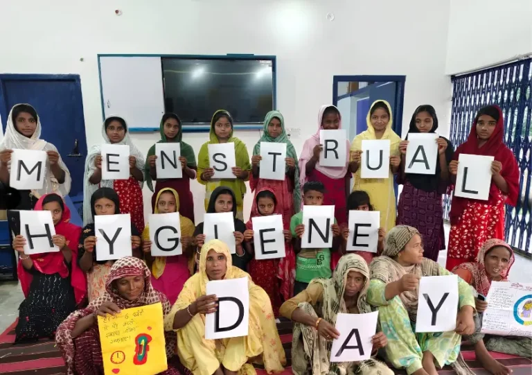 Rural women and adolescent girls holding letters spelling Menstrual Hygiene Day during an awareness workshop by BJUP, a Menstrual Hygiene Awareness NGO in Bihar.