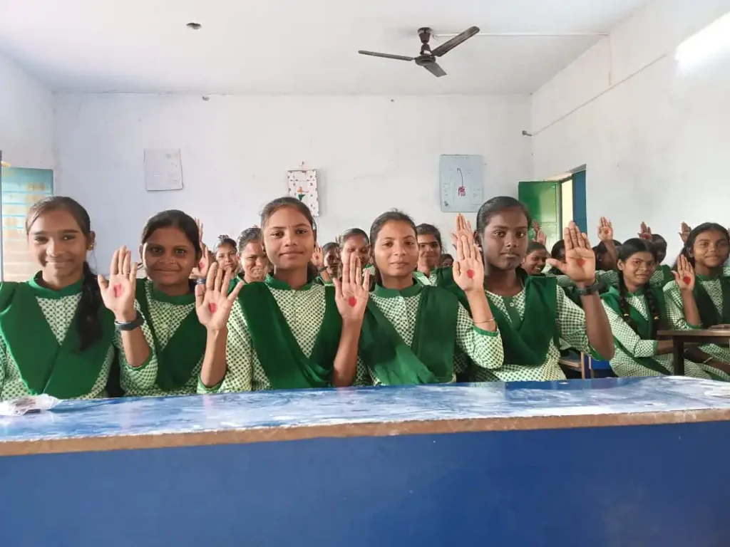 Schoolgirls in rural Bihar raising hands with red palm dots during a Menstrual Hygiene Management (MHM) awareness session in school.